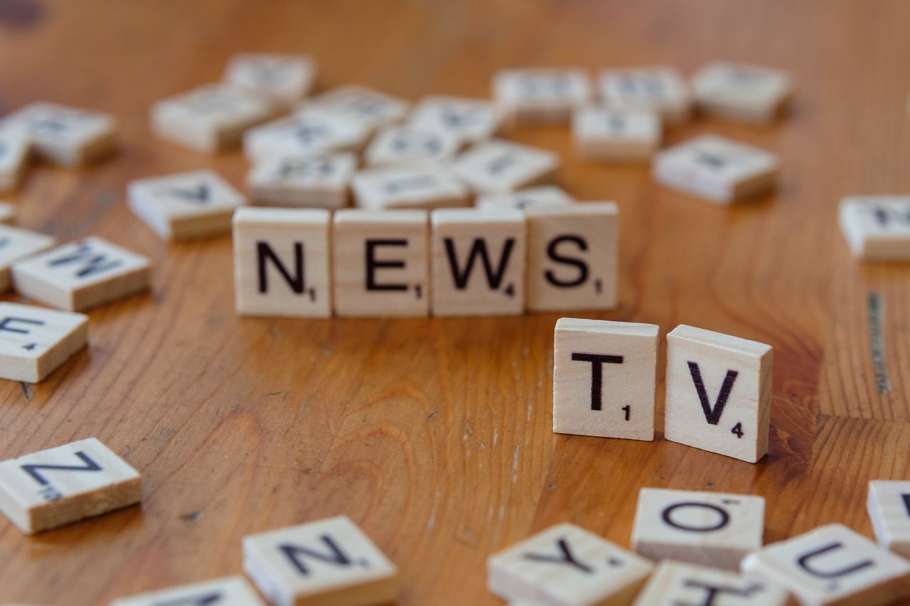 Close-up of Scrabble tiles spelling News and TV on a wooden surface.