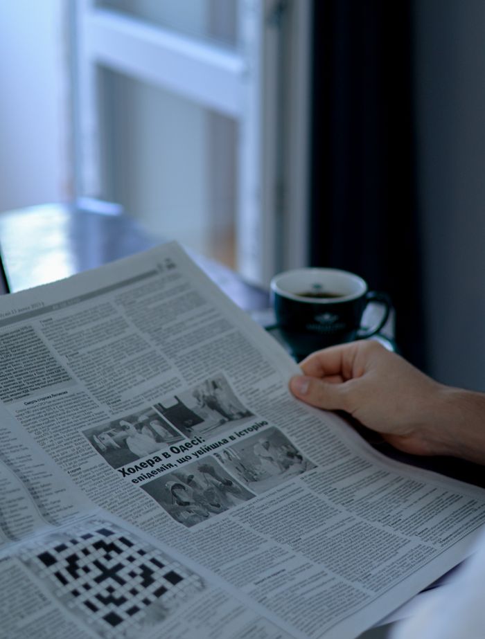 Person enjoying a quiet morning reading the newspaper with a cup of coffee by the window.